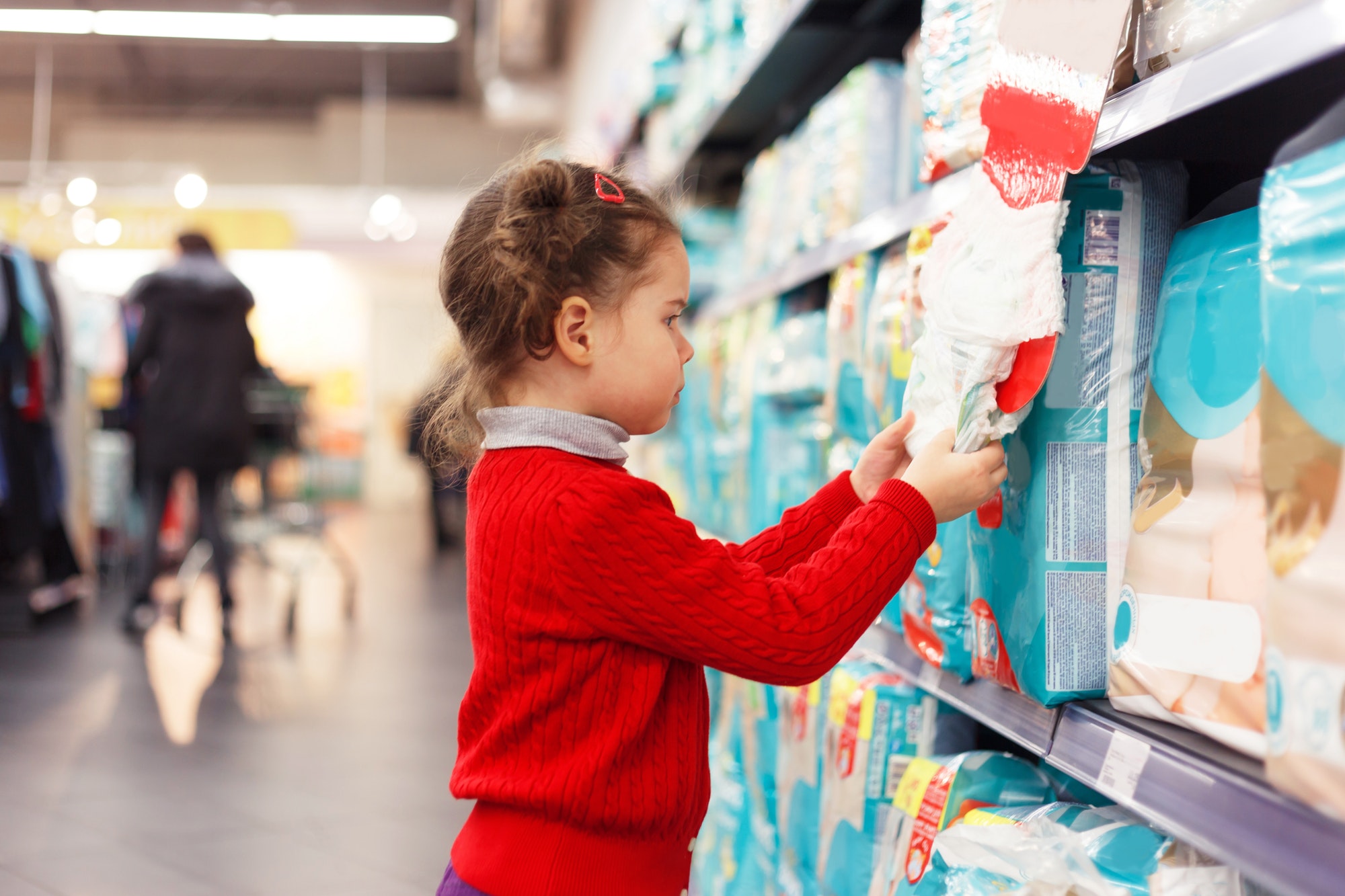 Little girl selects diapers in supermarket